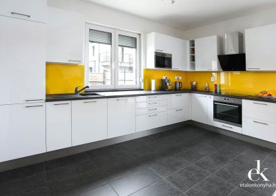 Magasfényű fehér konyhabútor, beton hatású pulttal és vidám sárga üveghátfallal